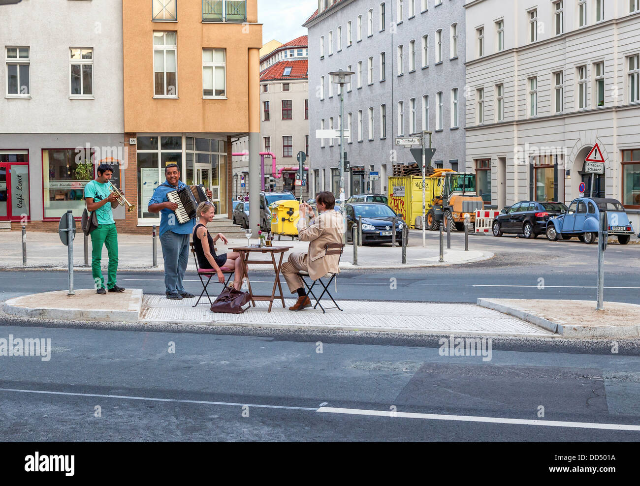 Un couple habillés sont divertis par des musiciens de rue tout en dînant sur l'îlot central d'une rue, Torstrasse - Berlin Banque D'Images