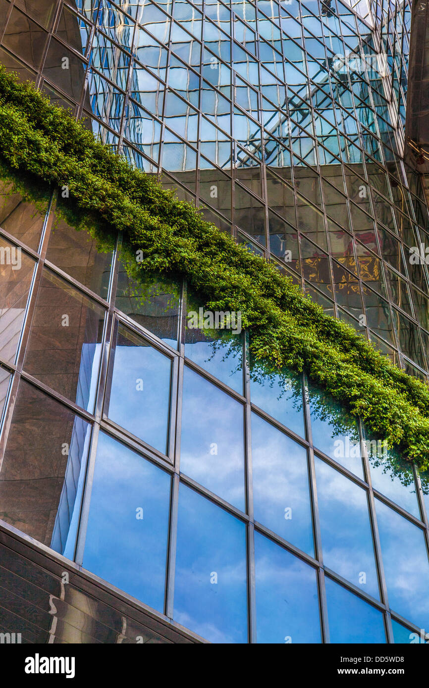 Un bâtiment moderne de verre avec reflet du ciel bleu et la verdure des plantes. Banque D'Images