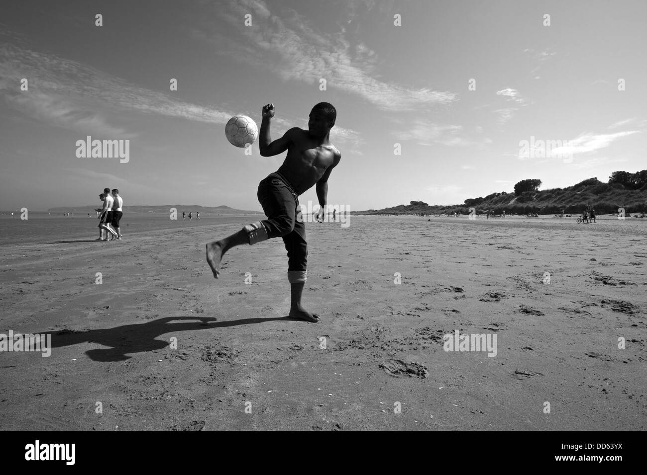 Un jeune homme jouant au football sur la plage. Banque D'Images