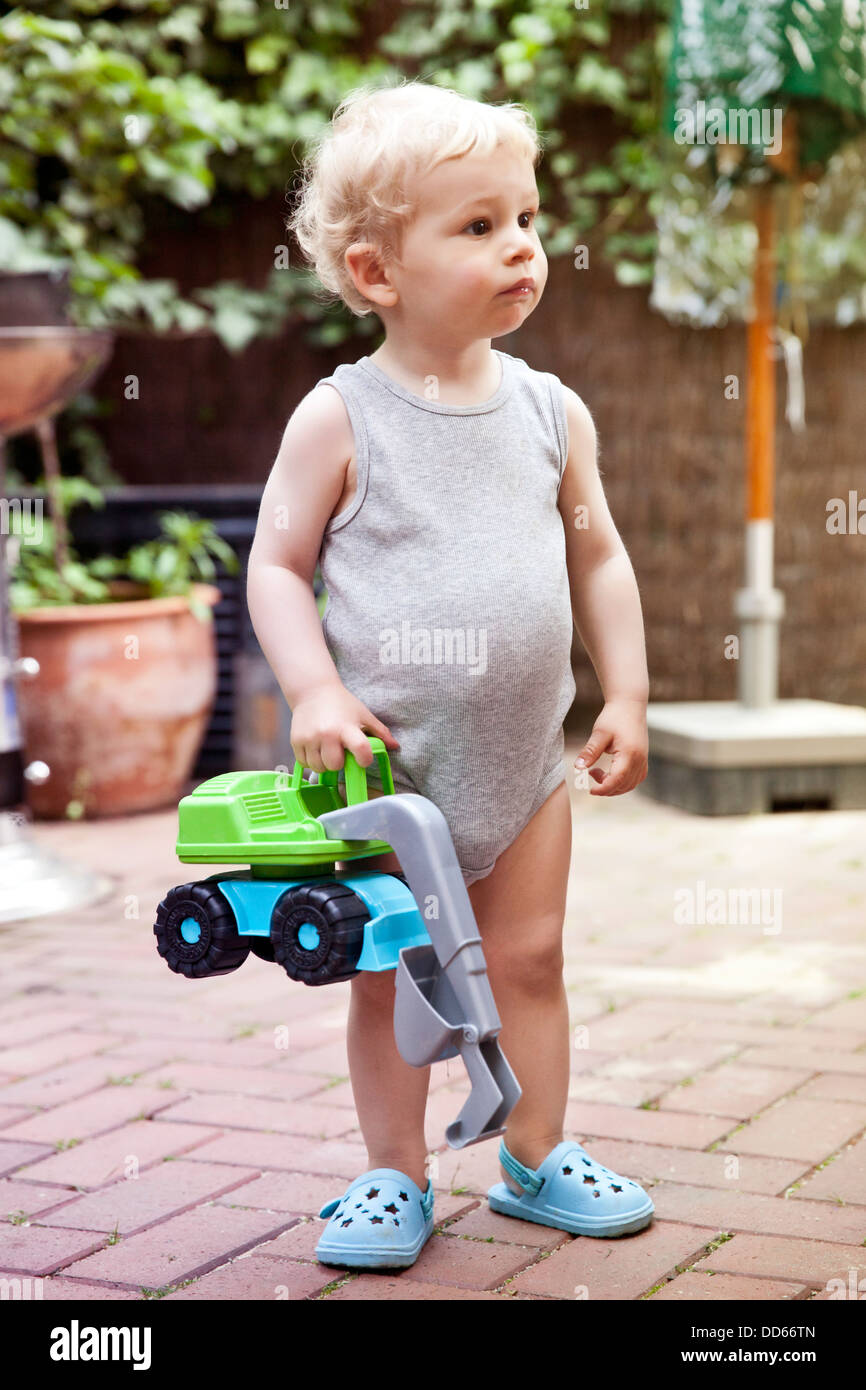 Allemagne, Bonn, Baby Boy standing in backyard with toy digger Banque D'Images