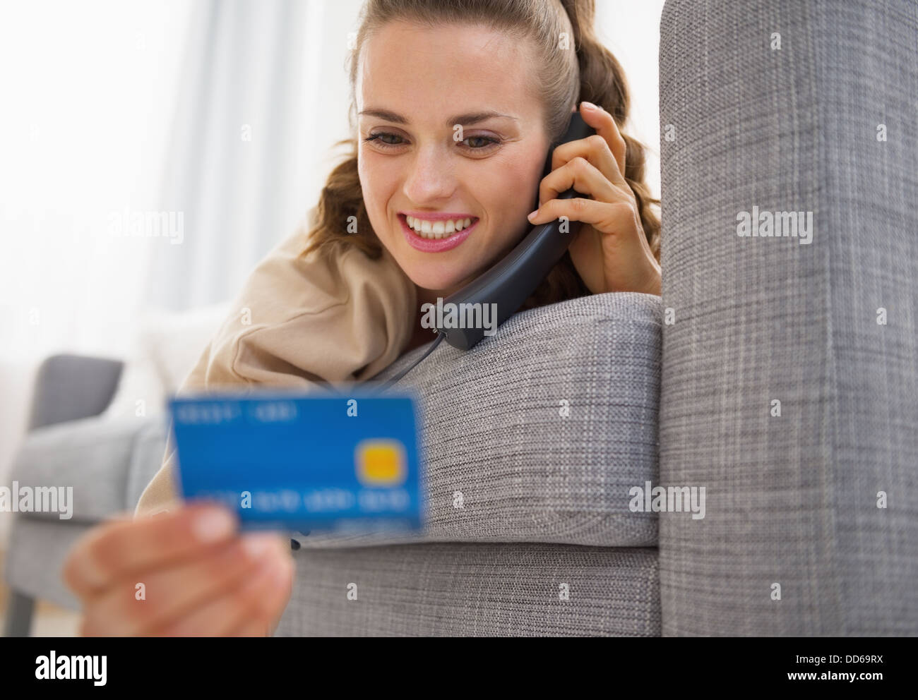 Jeune femme avec carte de crédit portant sur le canapé et parler phone Banque D'Images
