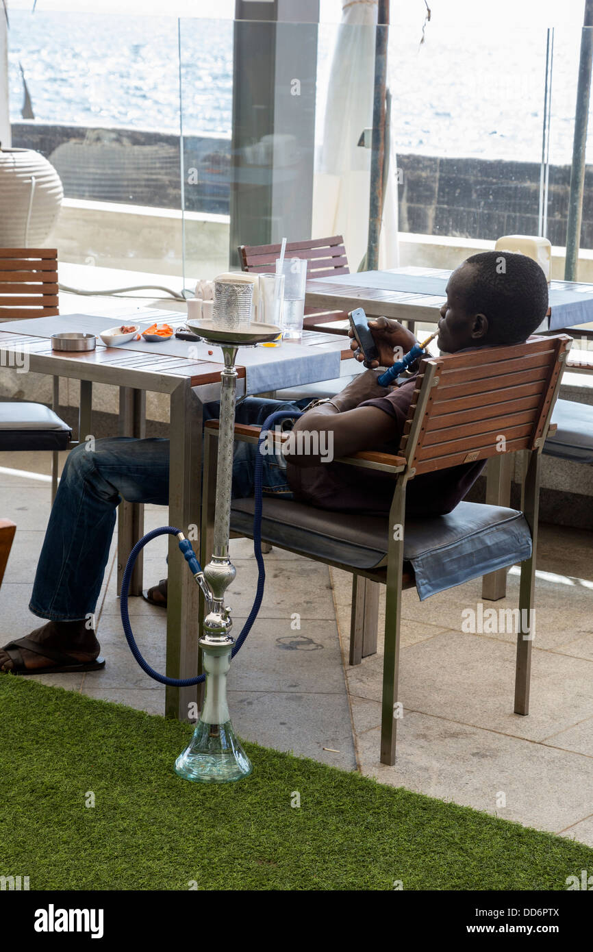Dakar, Sénégal. Client avec une chicha (pipe à eau) et du téléphone cellulaire dans un café-restaurant dans un centre commercial moderne. Banque D'Images