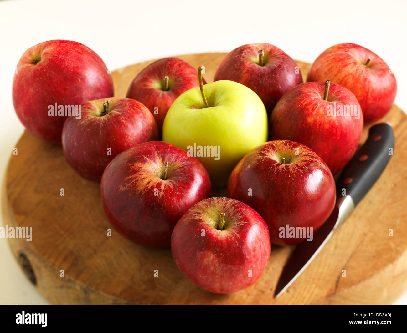 Un tas de pommes rouges disposées en triangle avec la pomme verte au milieu et un couteau sur la planche à découper. Banque D'Images