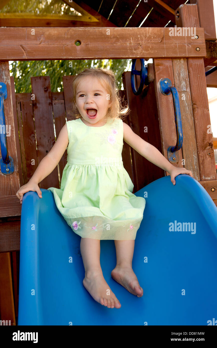 Deux ans, fille, et remplies sur la diapositive qui bleu attaché à l'aire de jeux en bois Banque D'Images