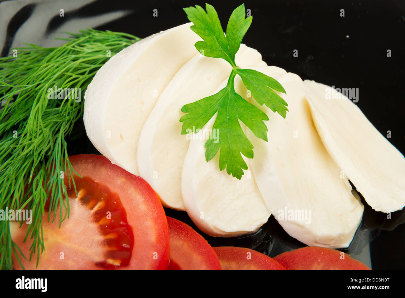 Tranches de fromage mozzarella à la plaque noire avec tomates et fines herbes Banque D'Images