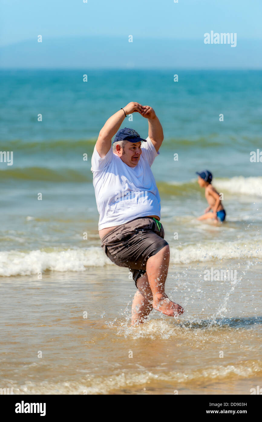 Un grand homme danse dans les vagues sur la plage de Bournemouth en Angleterre. Banque D'Images