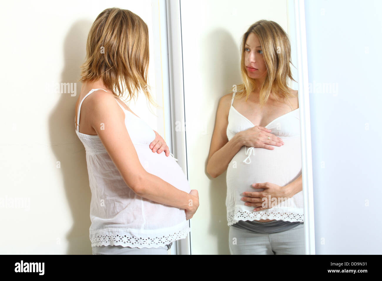 Femme enceinte regarde son reflet dans un miroir Autorisation Modèle disponible Banque D'Images
