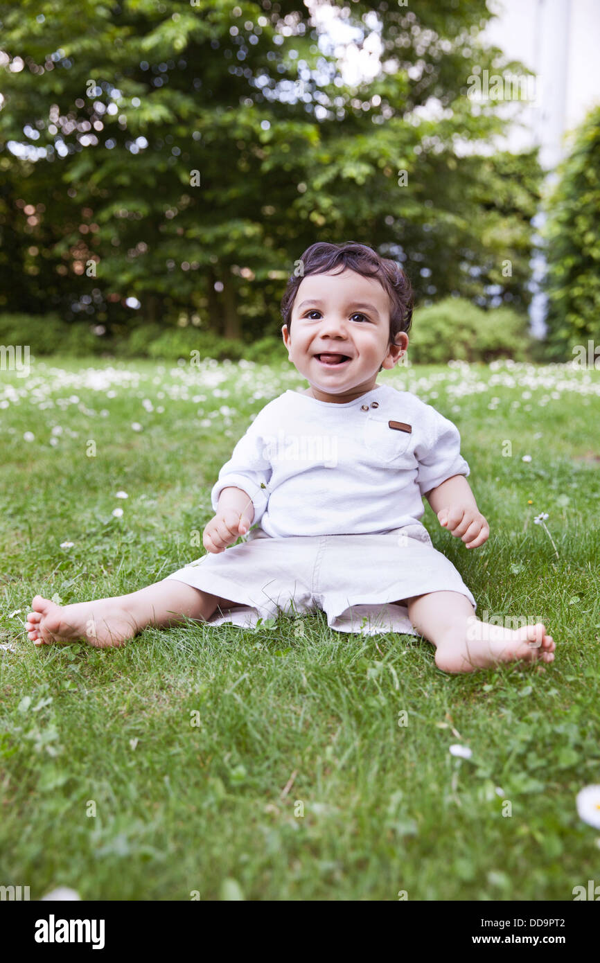 Baby Boy sitting on grass et holding daisy flower, smiling Banque D'Images