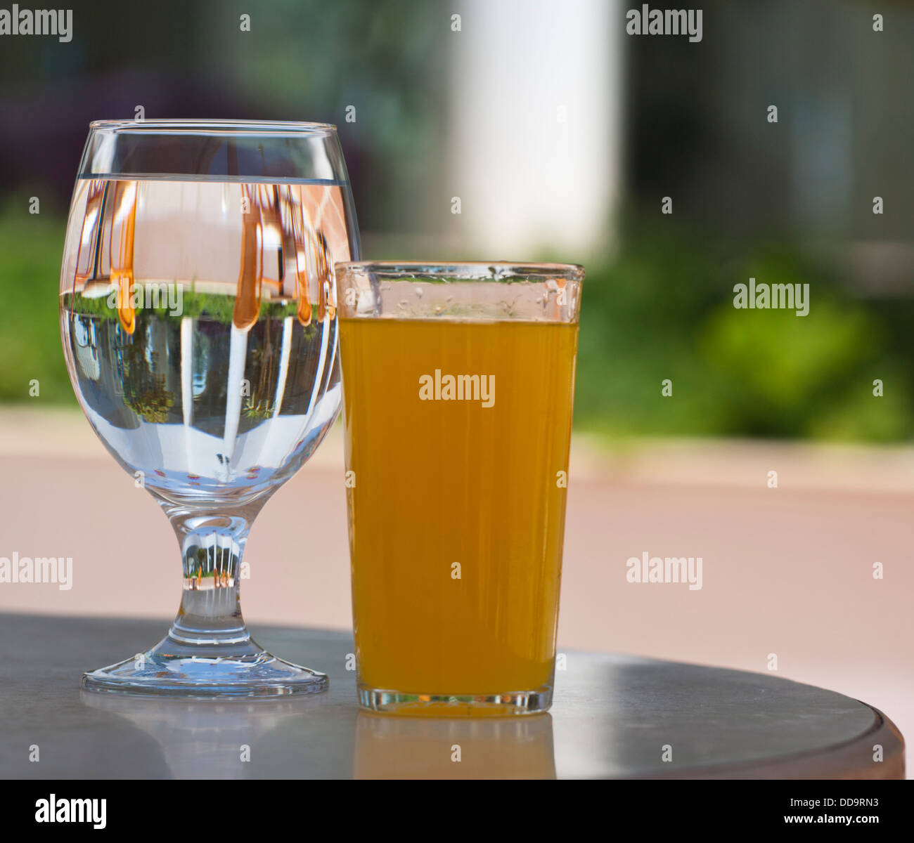Relections dans un verre d'eau sur une table d'extérieur avec le jus d'orange floue au premier plan Banque D'Images