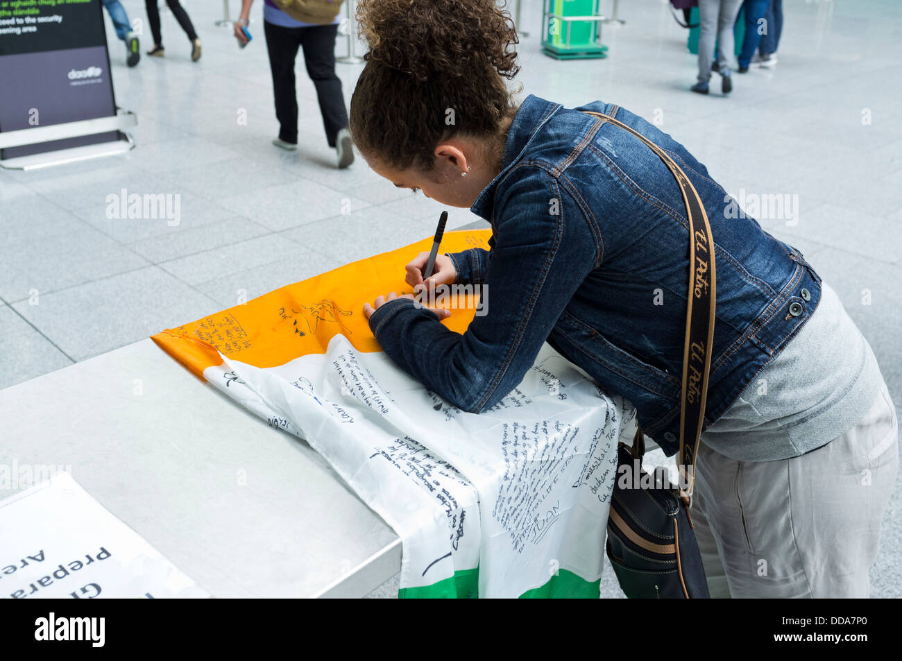 Jeune fille écrit sur un drapeau irlandais à l'aéroport de Dublin, Irlande. Banque D'Images