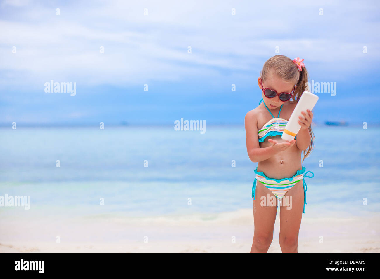 Adorable petite fille en maillot de bain est titulaire d'une lotion solaire bouteille Banque D'Images