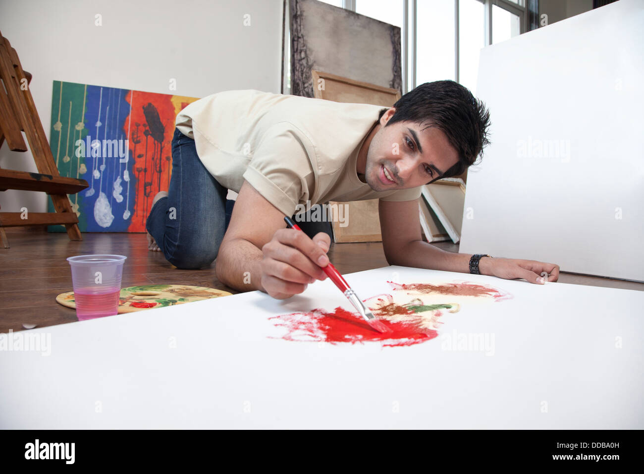Jeune homme souriant tandis que la peinture sur une grande toile à un studio d'art Banque D'Images