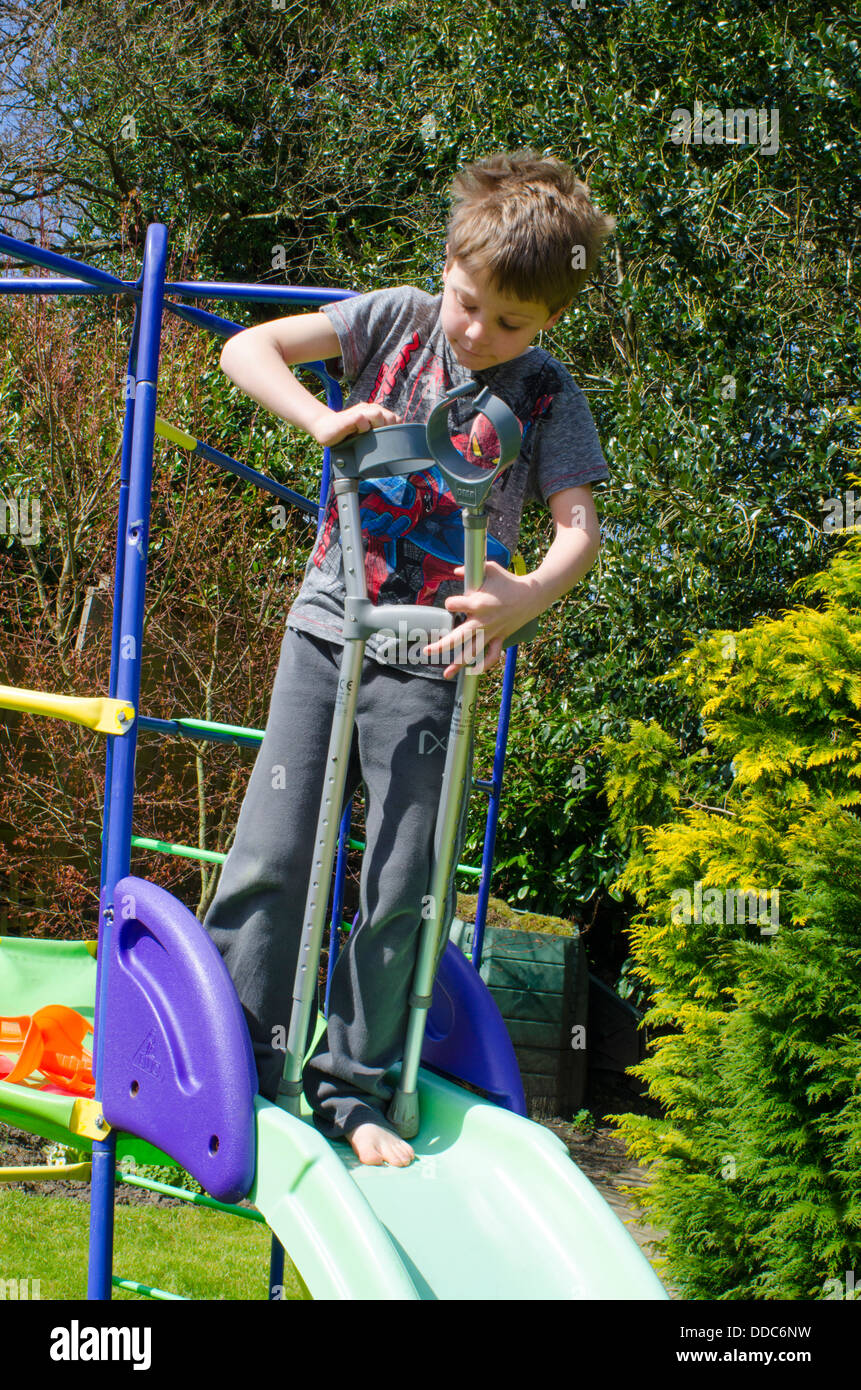 Garçon de huit ans avec des béquilles pense à être aventureux sur un jardin. Banque D'Images