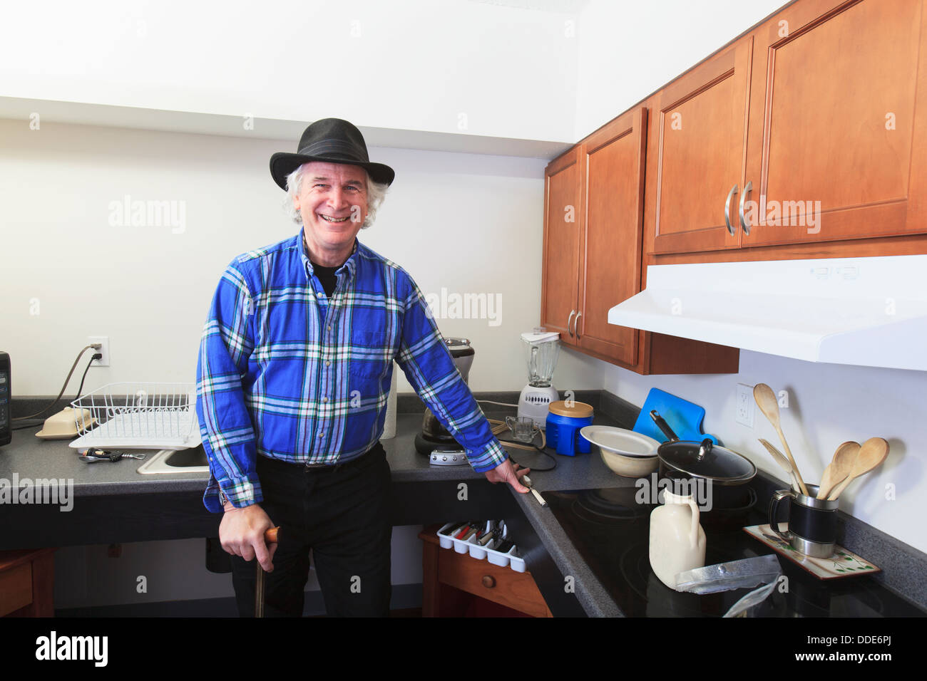 L'homme avec la sclérose en plaques debout dans sa cuisine accessible avec une canne Banque D'Images