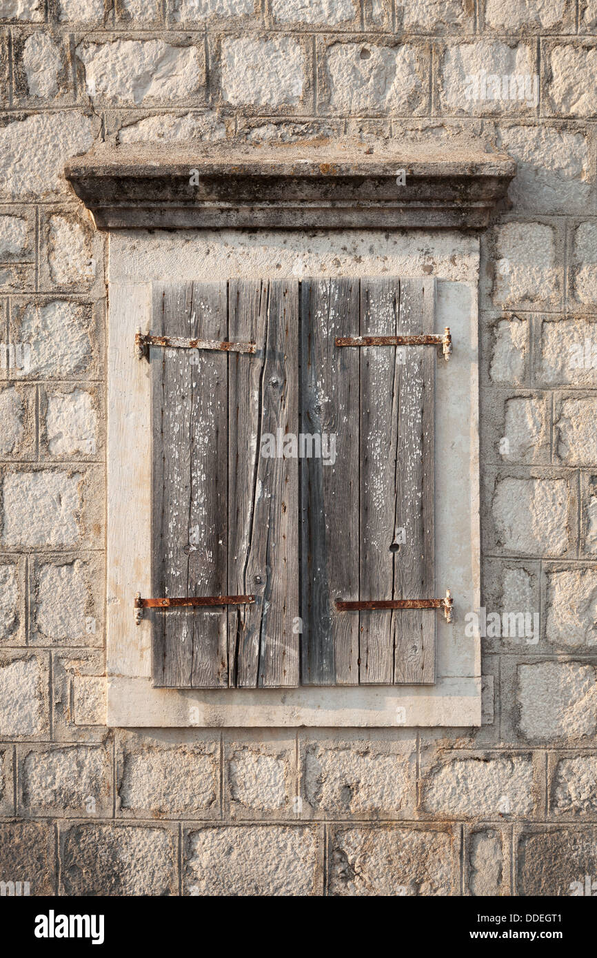 Fenêtre ancienne en bois fermée avec jalousies dans mur de pierre grise. La ville de Perast, Monténégro Banque D'Images