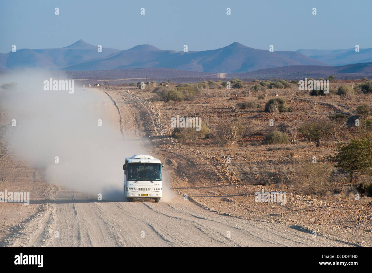 Bus touristique roulant dans un nuage de poussière sur un large chemin de gravier poussiéreux, région de Kunene, Namibie Banque D'Images
