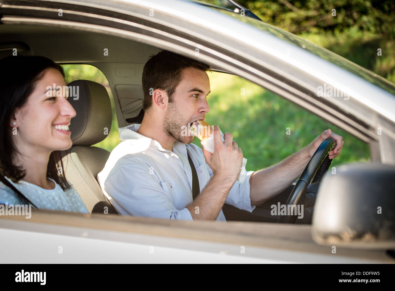 Couple en voiture - l'homme est au volant et de manger la baguette Banque D'Images