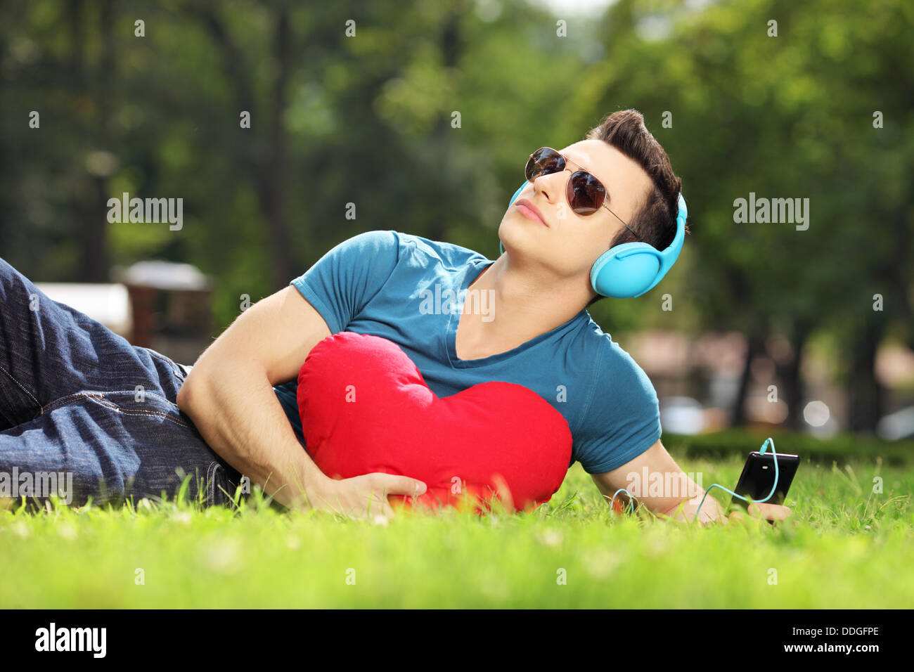 Beau mâle allongé sur une herbe avec coeur rouge listening music Banque D'Images