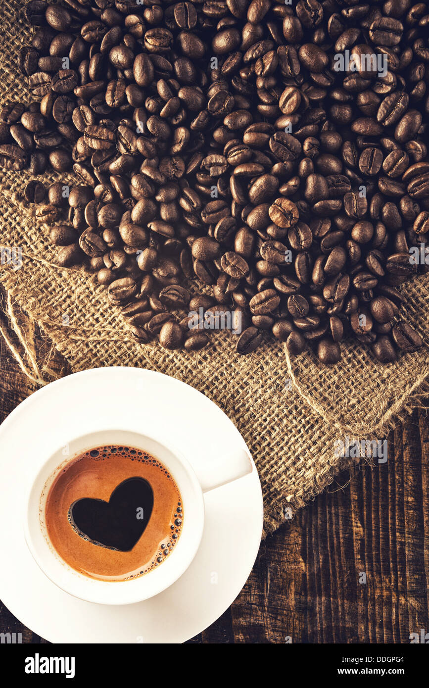 Les grains de café et tasse de café avec de la mousse en forme de coeur en toile de jute sur la texture. Banque D'Images