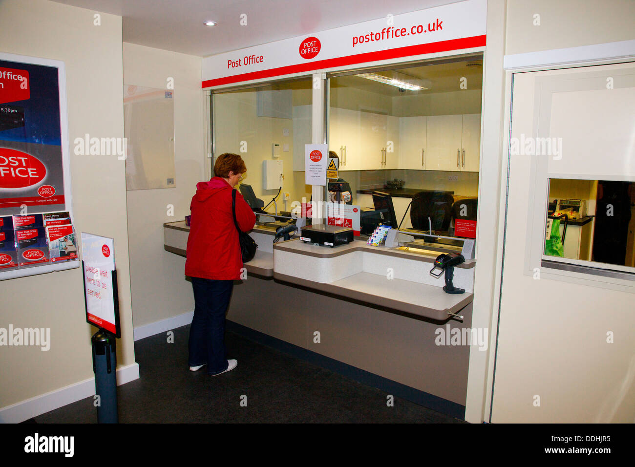 Woman in red jacket au guichet d'un office de poste Banque D'Images