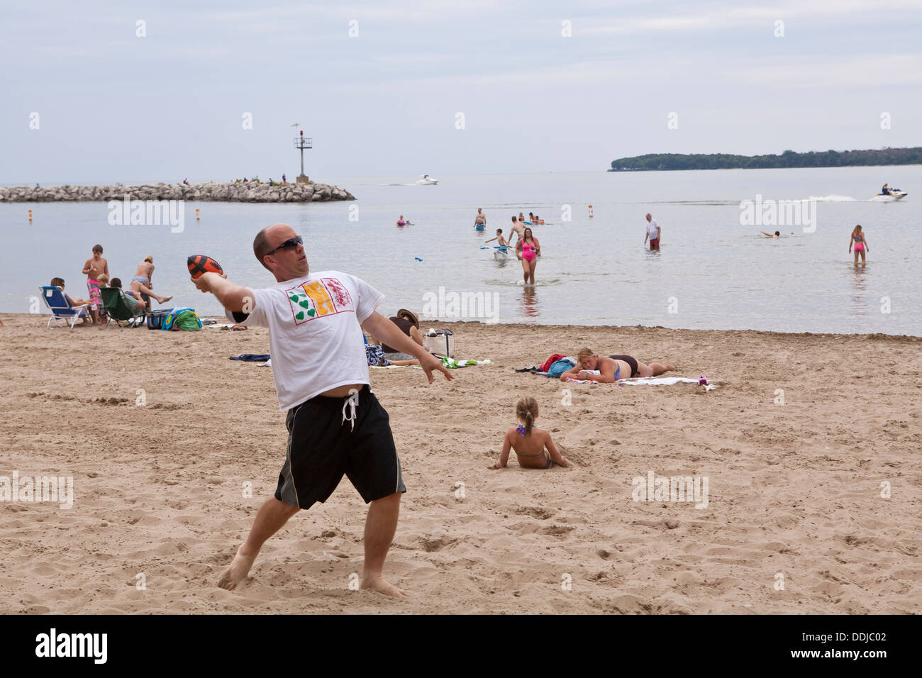 Un homme lance un ballon de football sur une plage de sable à l'île Kelleys State Park, Ohio Banque D'Images