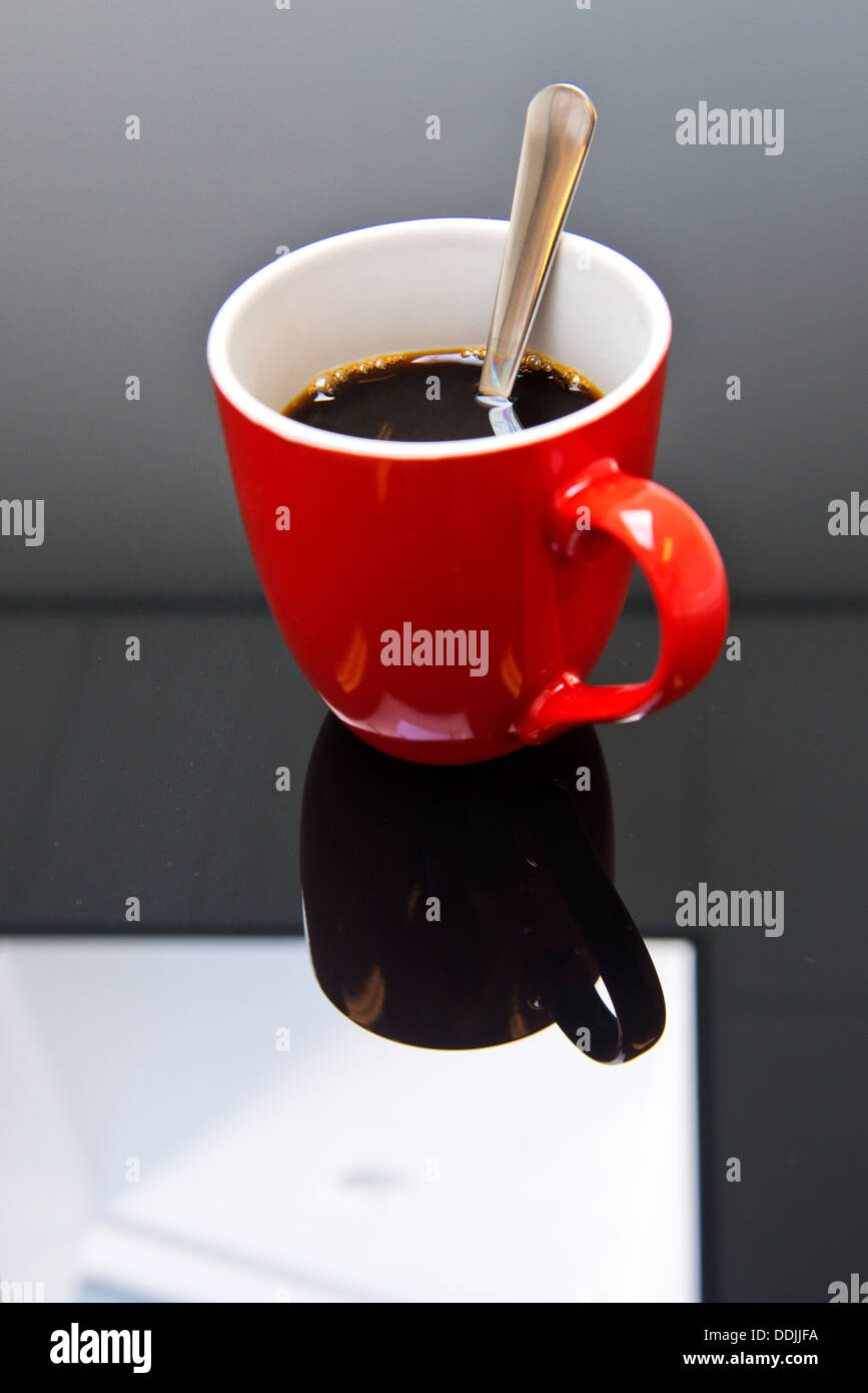 Tasse de café sur une table en verre noir, reflétant la lucarne dans le toit d'une salle de conférence Banque D'Images