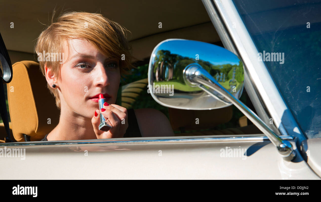 Jeune femme mise sur le rouge à lèvres dans le rétroviseur d'une voiture oldtimer classic Banque D'Images
