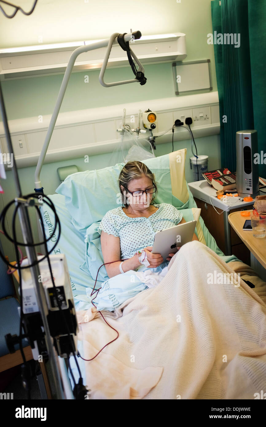 Une femme d'âge moyen, de récupérer son iPad lecture sur un lit d'hôpital après une opération un remplacement de la hanche à un hôpital du NHS Wales UK Banque D'Images