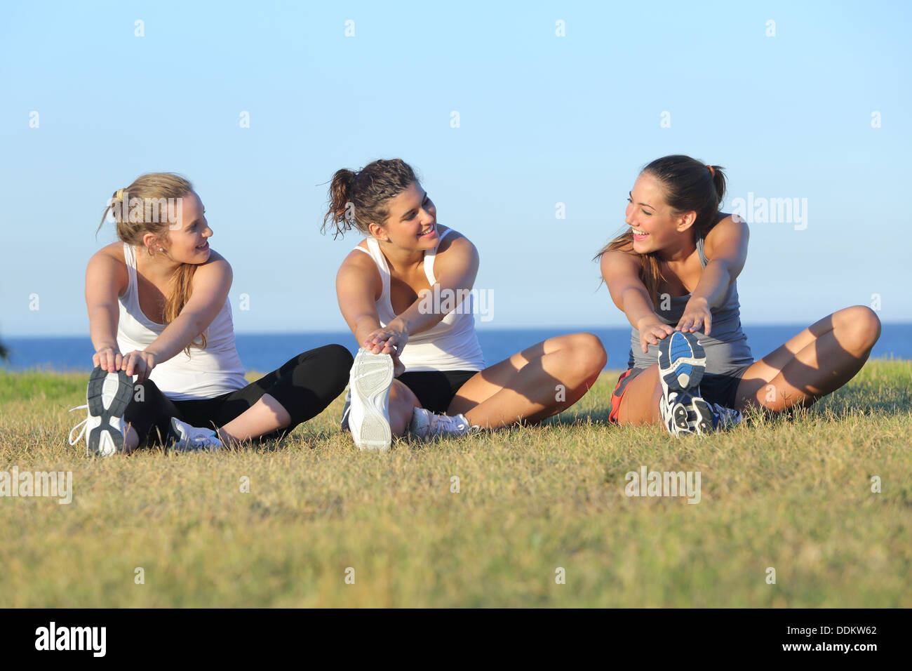 Groupe de trois femmes qui s'étend après le sport sur l'herbe avec la mer en arrière-plan Banque D'Images