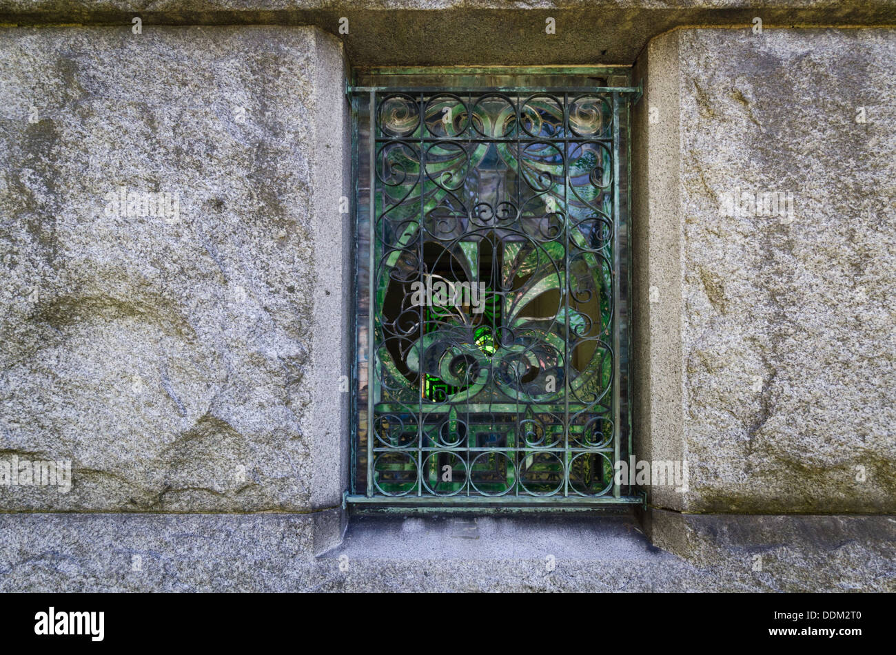 Fenêtre cassée dans un mausolée avec des volutes en fer forgé et vitraux décoratifs. Banque D'Images