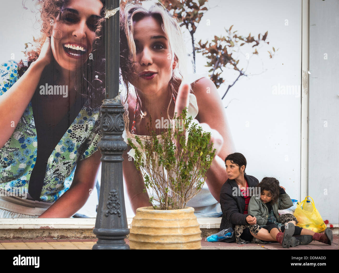 Femme et la mendicité des enfants roms à côté d'un panneau publicitaire Publicité dans la ville provinciale de Rovetta, Péloponnèse, Grèce Banque D'Images