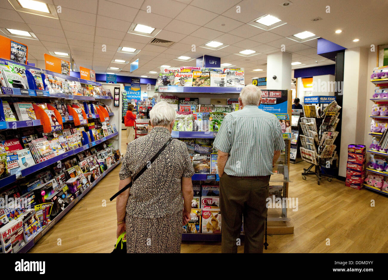 Un vieux couple retraités caucasiens shopping pour les magazines, marchand de WH Smith, UK Banque D'Images