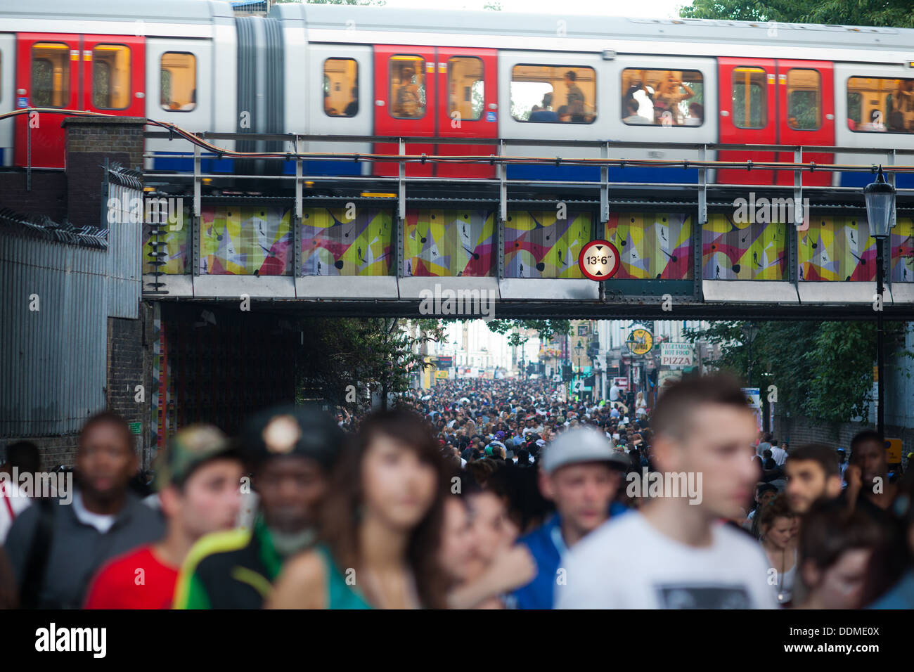 Portobello Road est imposé avec Carnival festivaliers au coucher du soleil. Un tube train passe au plafond de la lumière mourante. Banque D'Images