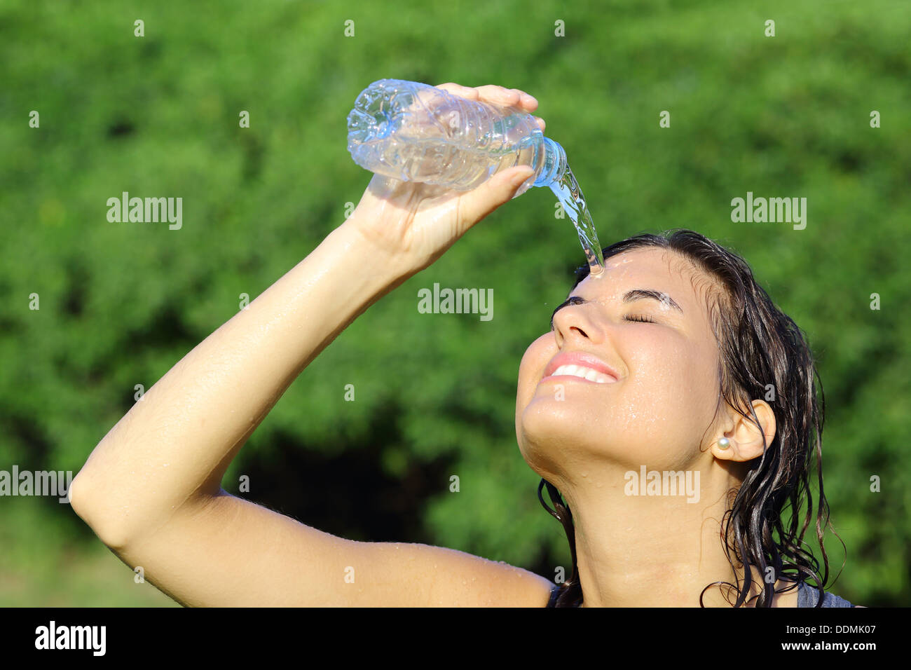 Jolie femme se jetant de l'eau d'une bouteille avec un fond vert Banque D'Images