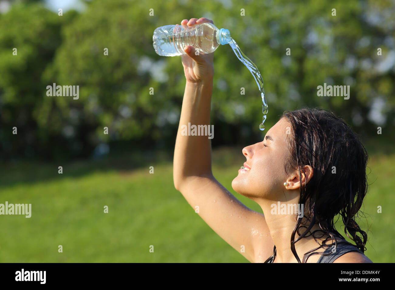 Belle femme se jetant de l'eau d'une bouteille avec un fond vert Banque D'Images