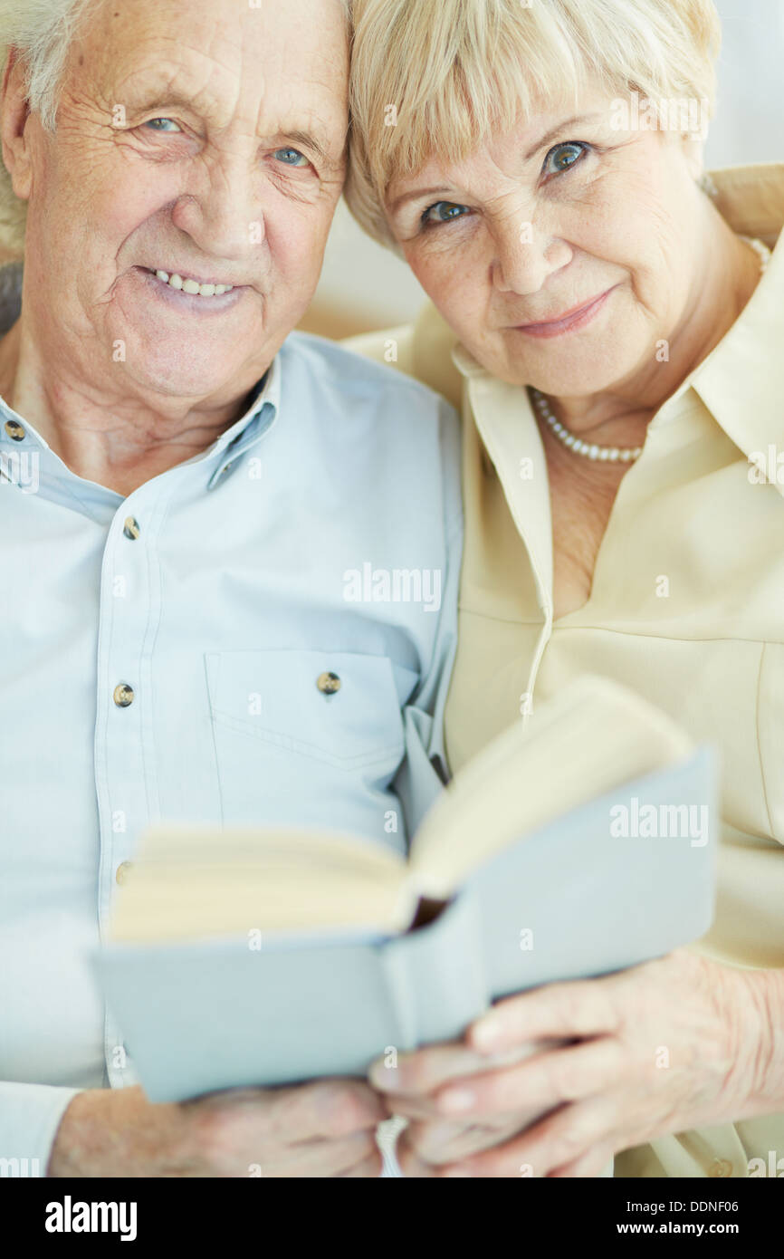 Portrait d'un franc senior couple looking at camera while reading book together Banque D'Images