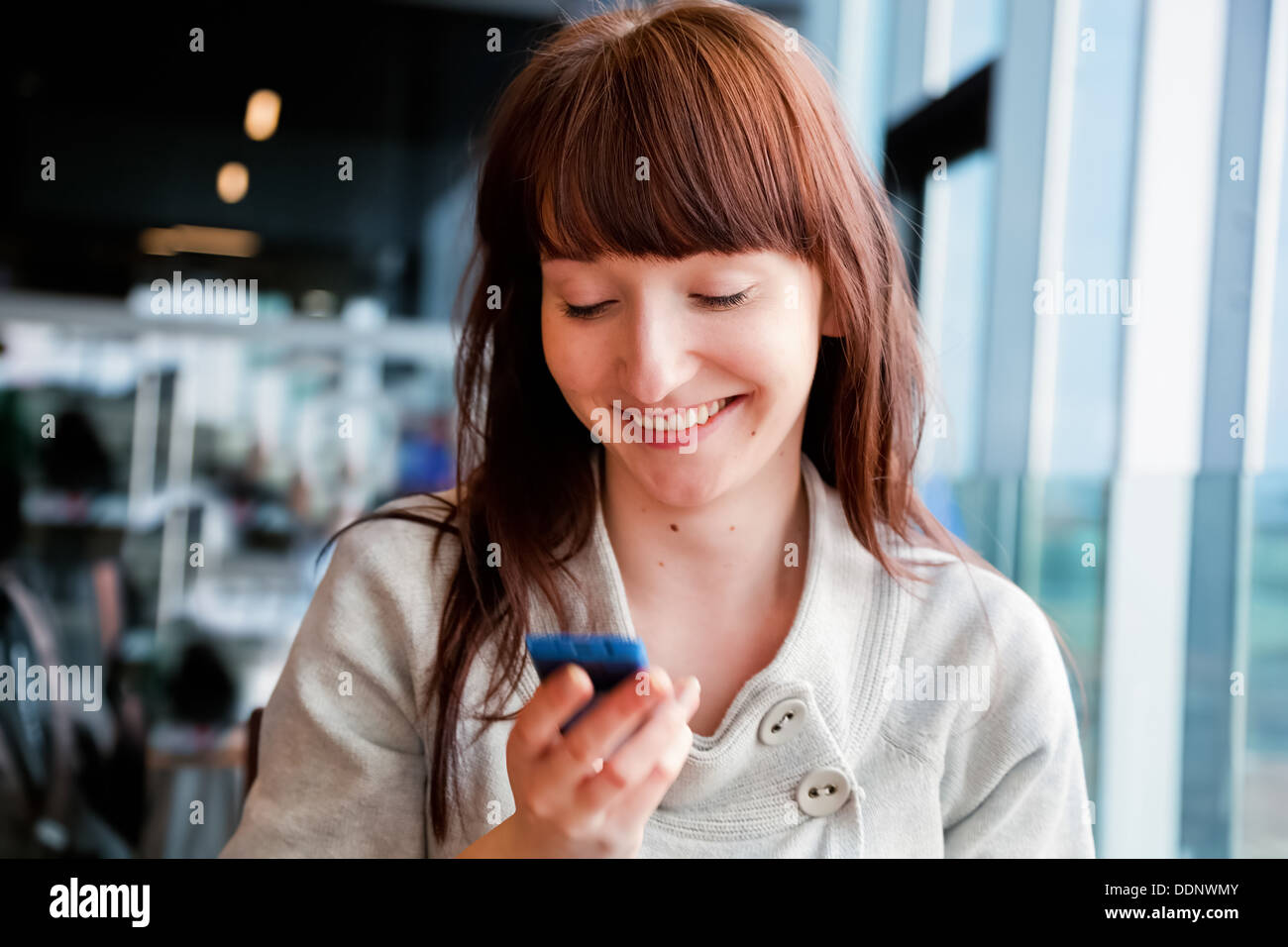 Femme textos sur téléphone mobile et souriant, assis dans un café Banque D'Images