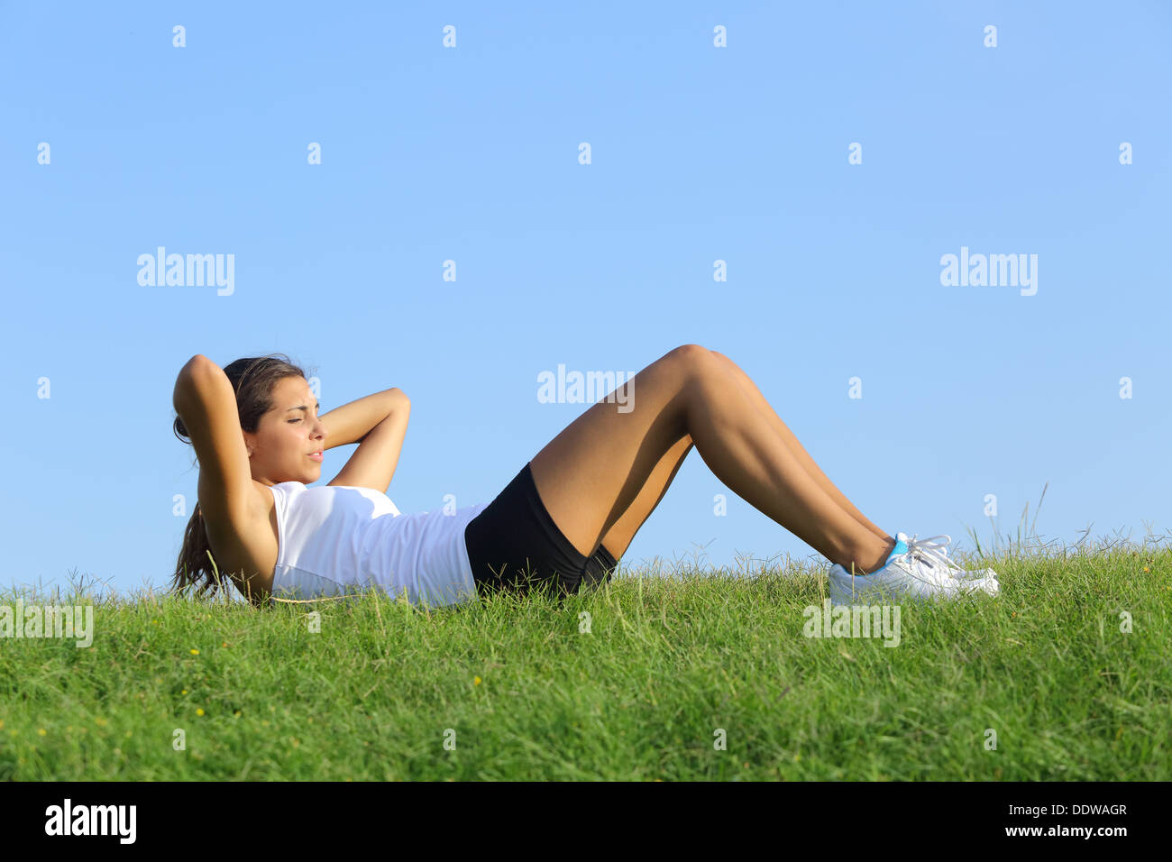 Jolie femme faisant des craquements sur l'herbe verte avec le ciel en arrière-plan Banque D'Images