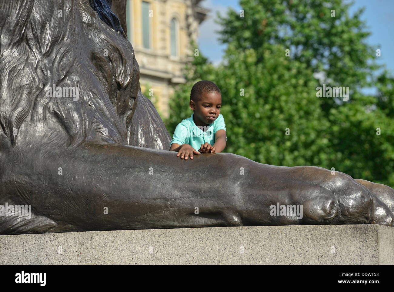Petit garçon afro-américain posant pour la photographie aux pieds d'un des lions à Trafalgar Square Banque D'Images