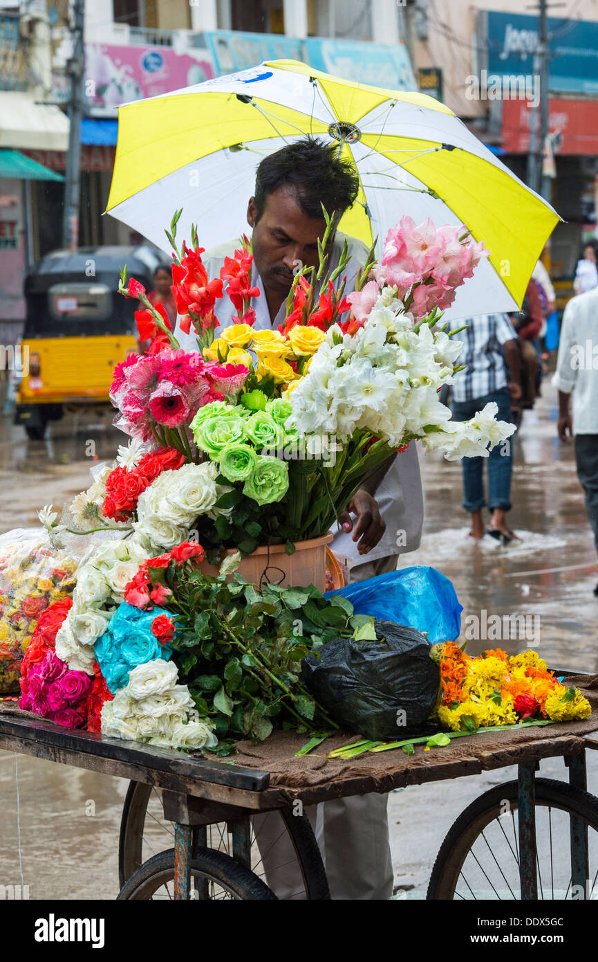 L'homme indien vente de fleurs à partir d'un panier sous la pluie. Puttaparthi, Andhra Pradesh, Inde Banque D'Images