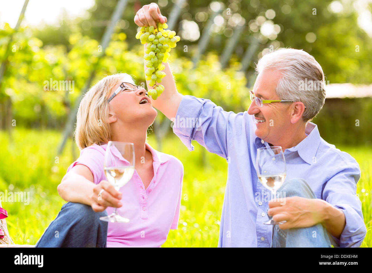 Couple de l'homme et de la femme ayant été pique-nique sur prairie de boire du vin dans la région de vineyard, il corrompt son épouse avec des raisins Banque D'Images