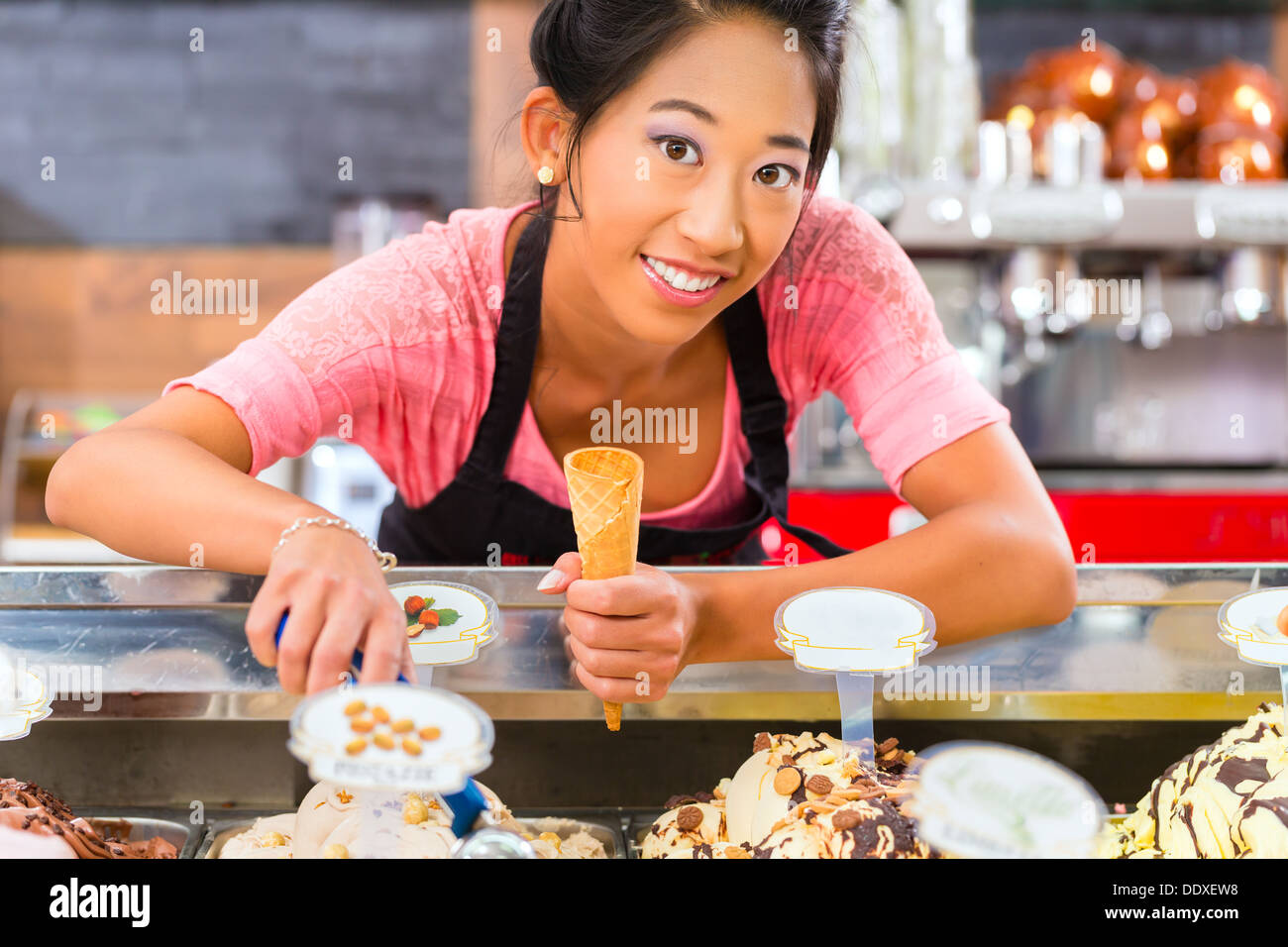 Jeune vendeuse asiatique dans un glacier prend une boule de crème glacée Banque D'Images