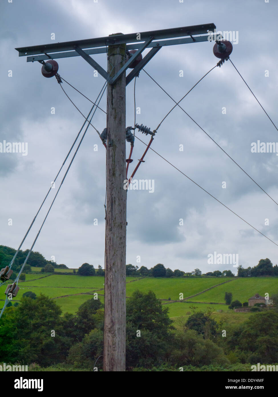 Pylône de l'électricité fixée contre green Rolling hills et un ciel nuageux. Banque D'Images