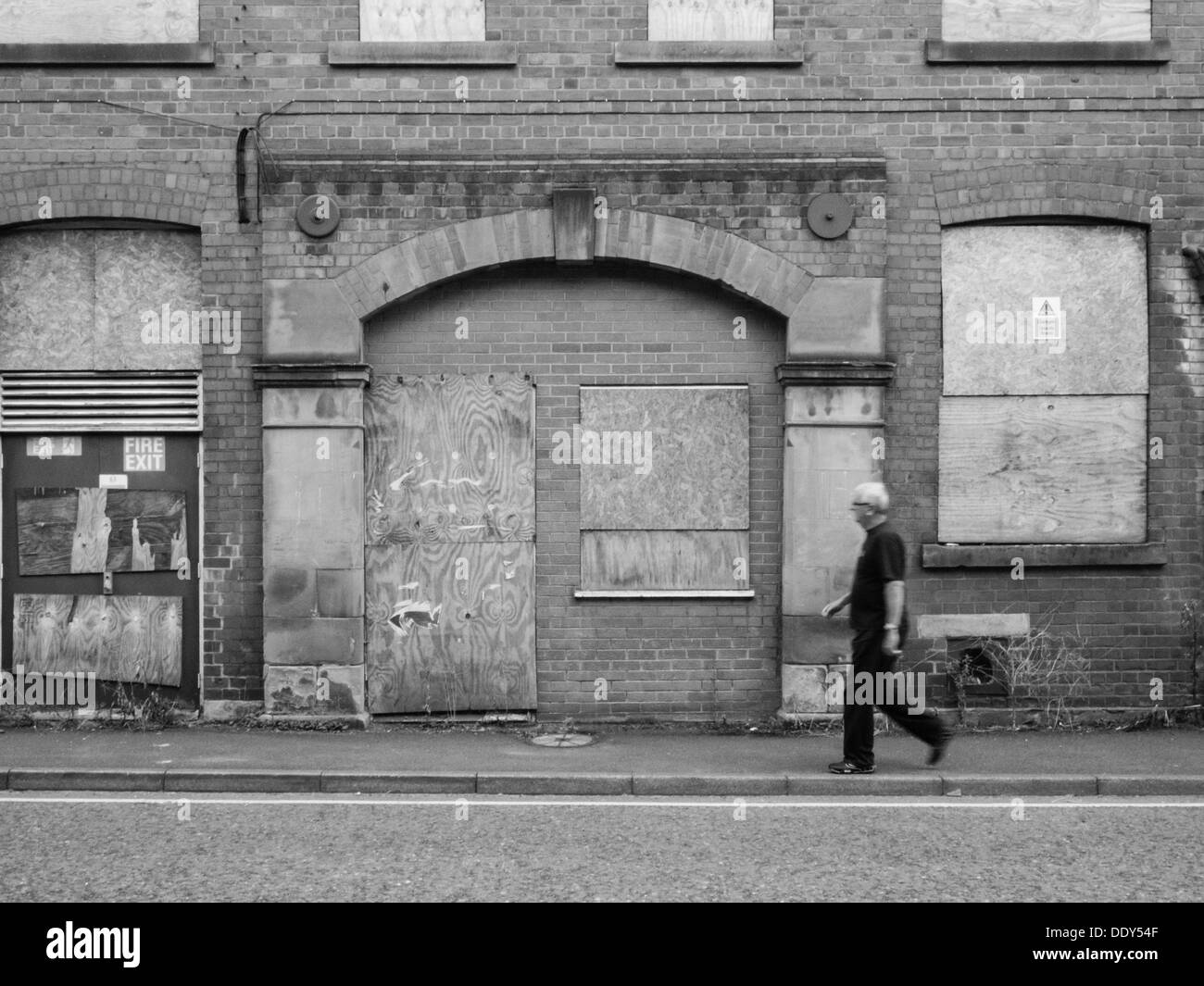 Homme marchant à travers l'armature devant une vieille usine abandonnée et abandonnés avec barricadèrent windows. Banque D'Images