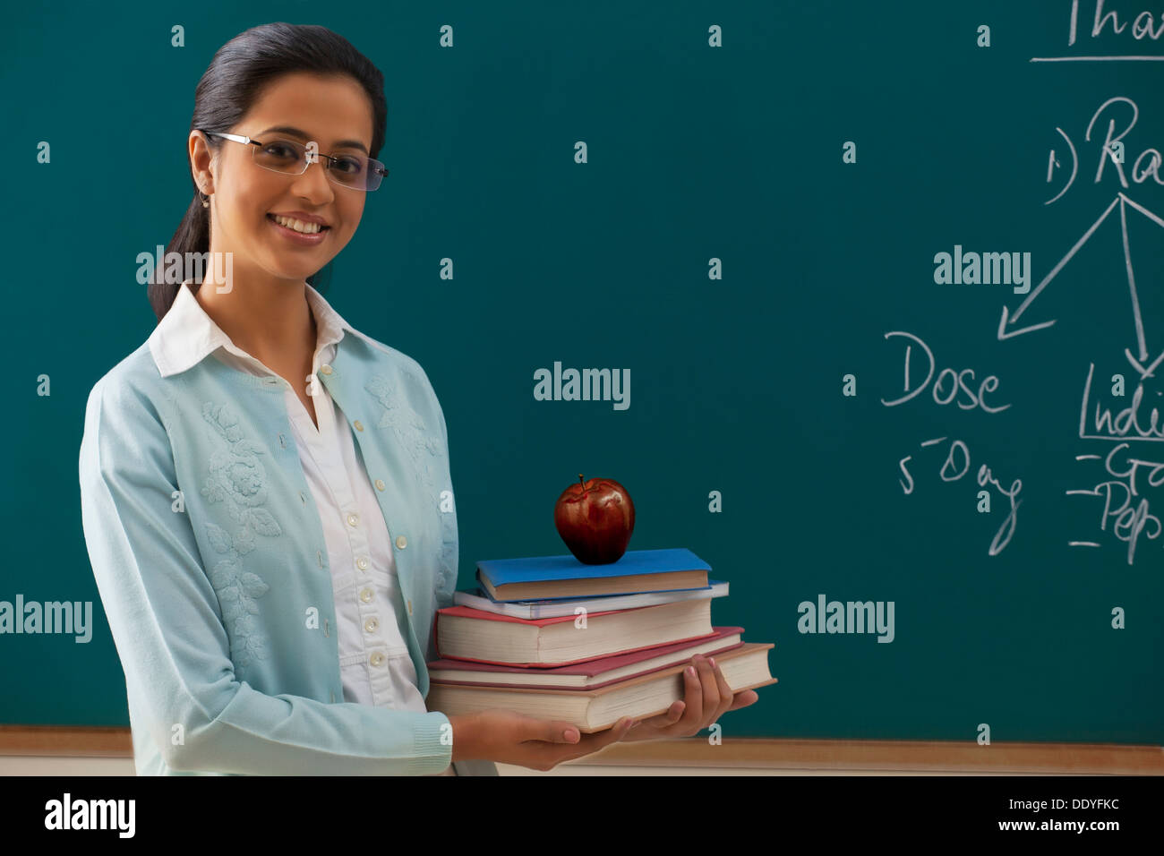 Portrait of young female teacher holding pile de livres contre chalkboard Banque D'Images