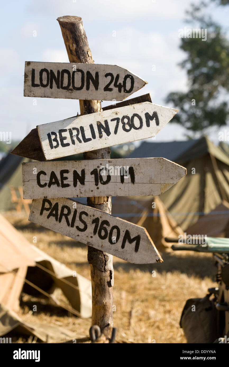 Poteaux de signalisation sur une branche la direction de Caen et Paris Berlin Londres avec tentes sur le terrain en arrière-plan Banque D'Images