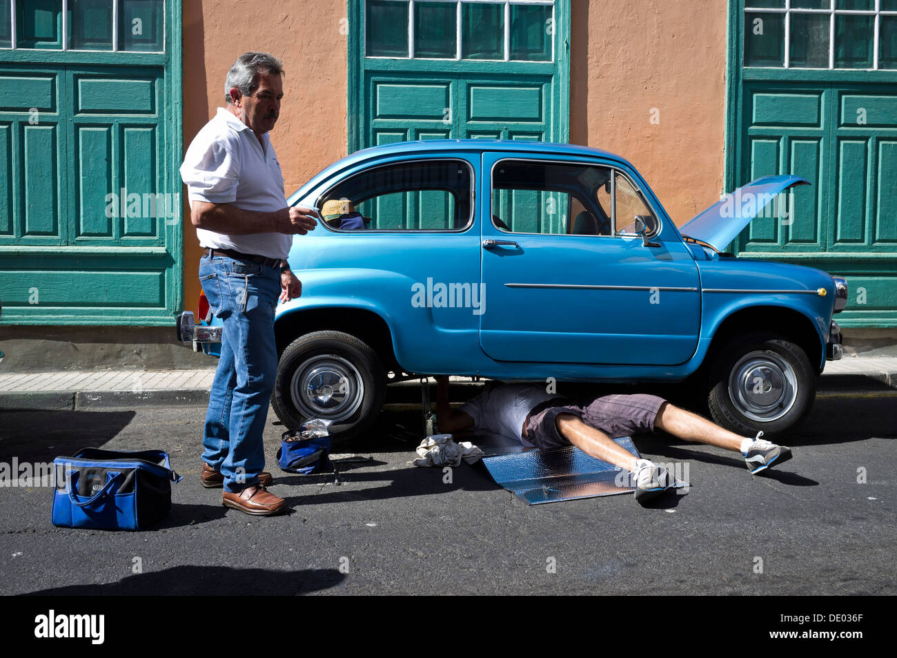 Seat 600 vintage car ventilées avec homme étendu sous les réparations exigées pendant qu'un autre regarde sur. Banque D'Images