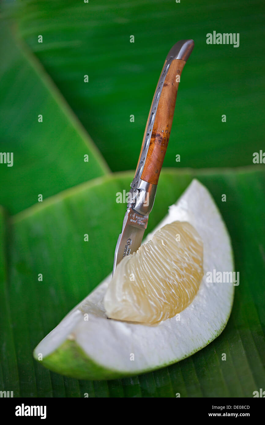 Couteau de poche se bloque dans un segment d'un pomelo fruit allongé sur une feuille de bananier Banque D'Images