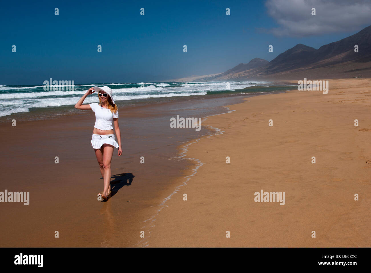 Femme marchant le long d'une plage de sable Banque D'Images