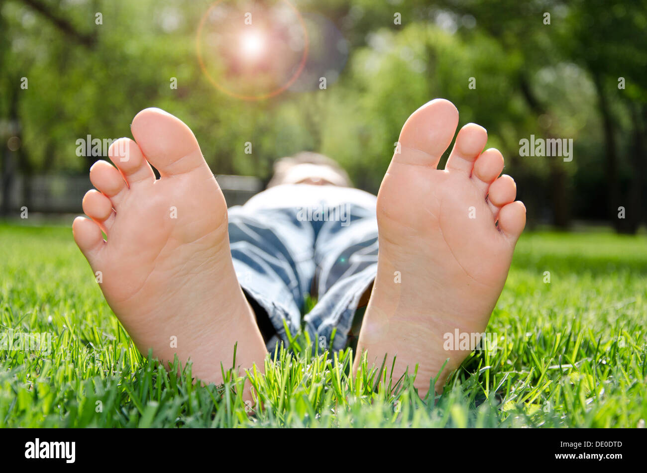 Une paire de pieds nus d'un petit garçon se détendre sous le soleil sur une pelouse verte Banque D'Images